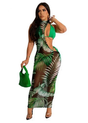 Woman wearing a tropical leaf print dress with a green handbag on a white background