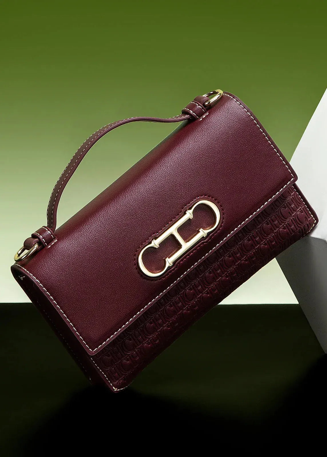 Maroon handbag with gold clasp on a green and white background