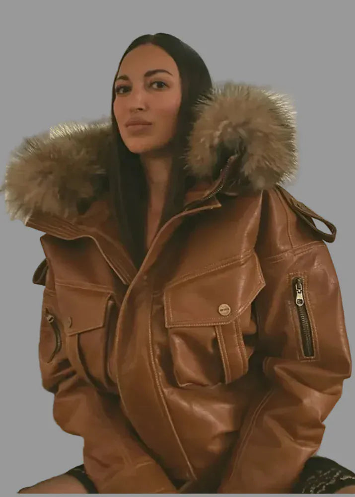 Person wearing a brown leather jacket with a fur-lined hood indoors.