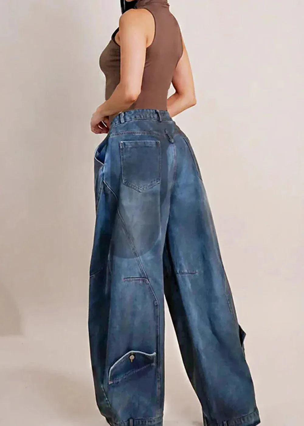 Person wearing a brown sleeveless top and blue wide-leg jeans on a plain background