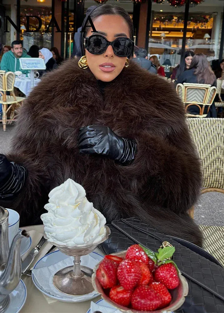 Person in a fur coat with a dessert and strawberries at an outdoor cafe.