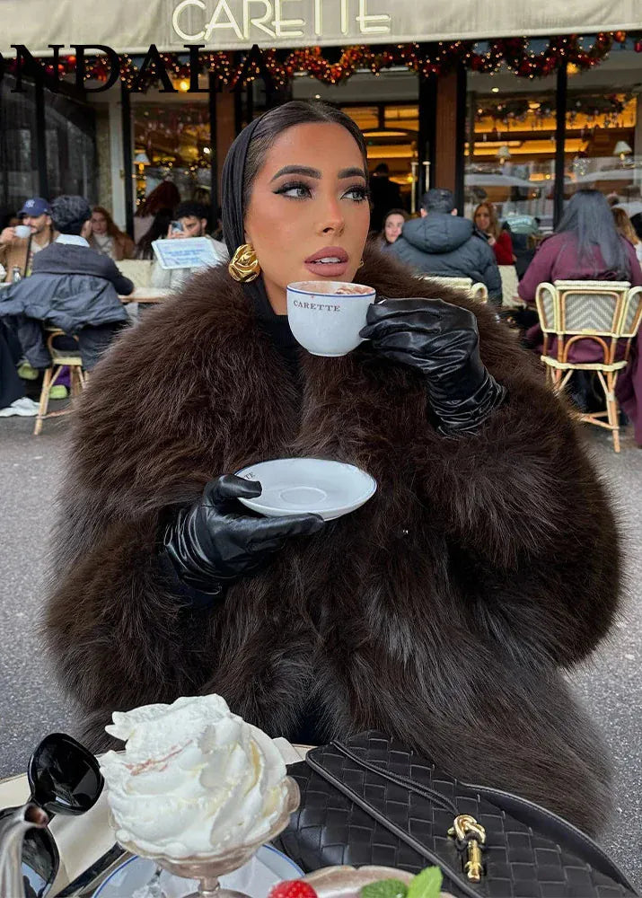 Woman in fur coat and gloves holding a cup and saucer outdoors with a cafe in the background