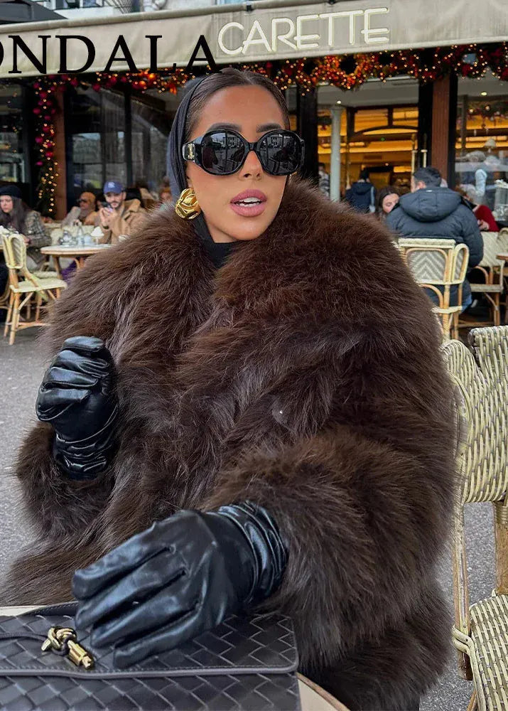Woman in a fur coat and sunglasses standing in front of a cafe named 'Kondalacarette'.