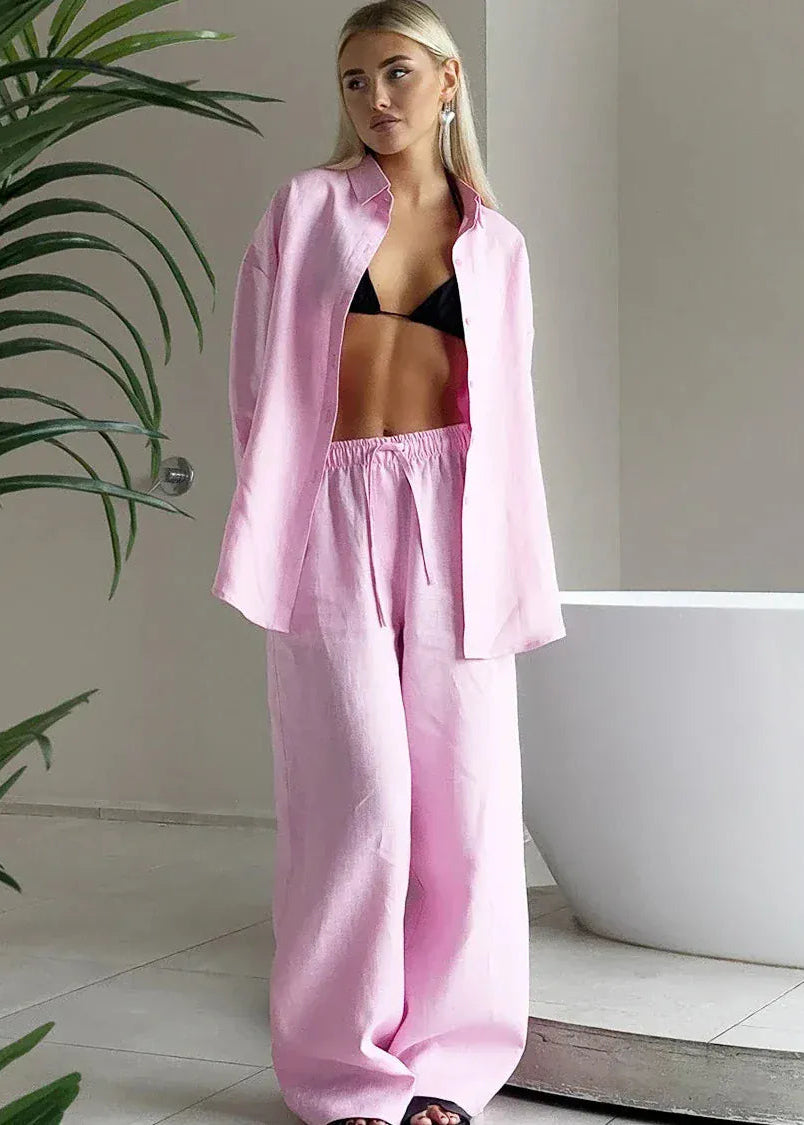 Woman wearing a pink outfit standing in a bathroom with a plant and bathtub in the background.