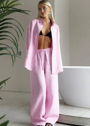 Woman wearing a pink outfit standing in a bathroom with a plant and bathtub in the background.
