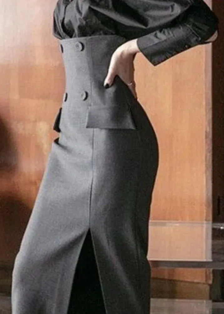 Person wearing a black outfit with a high-waisted pants and jacket against a wooden background