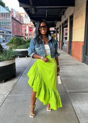 Woman in a bright green skirt and denim jacket standing on a city sidewalk.