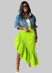 Woman in a bright green skirt and denim jacket standing on a city sidewalk.