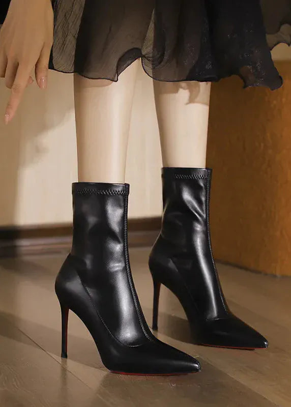 Black high-heeled boots worn with a sheer black skirt on a wooden floor.