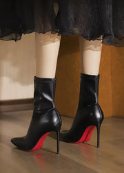 Black high-heeled boots with red soles worn by a person in a black dress.