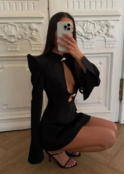 Person wearing a black dress with cut-out design in a room with decorative white wall.