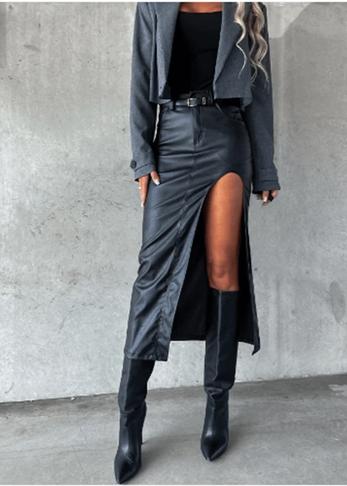 Person wearing a gray coat, black leather skirt, and black knee-high boots against a concrete wall.
