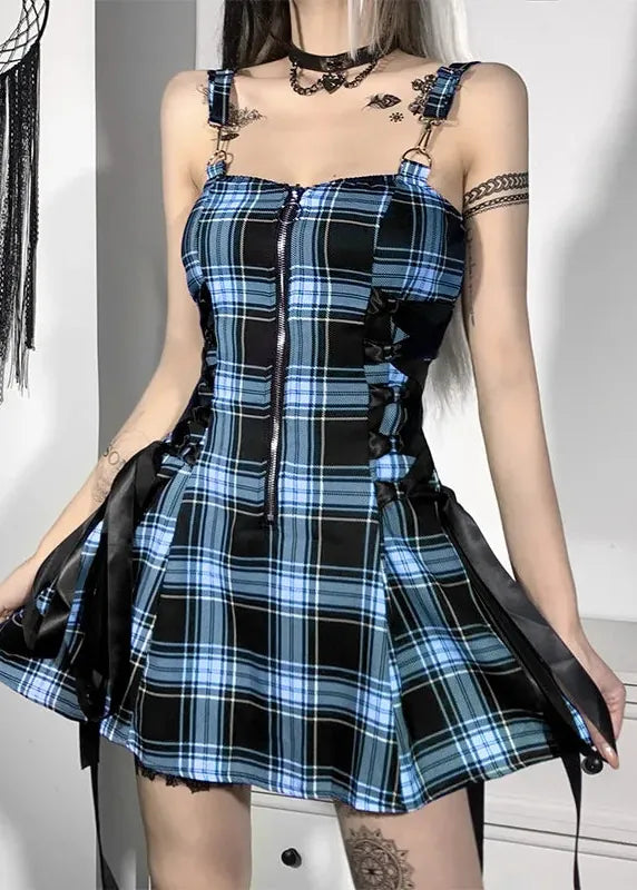 A model wearing a blue, black, and white plaid corset mini dress with black satin side panels, metal shoulder straps, and lace-up details, set against a white wall with gothic decor.