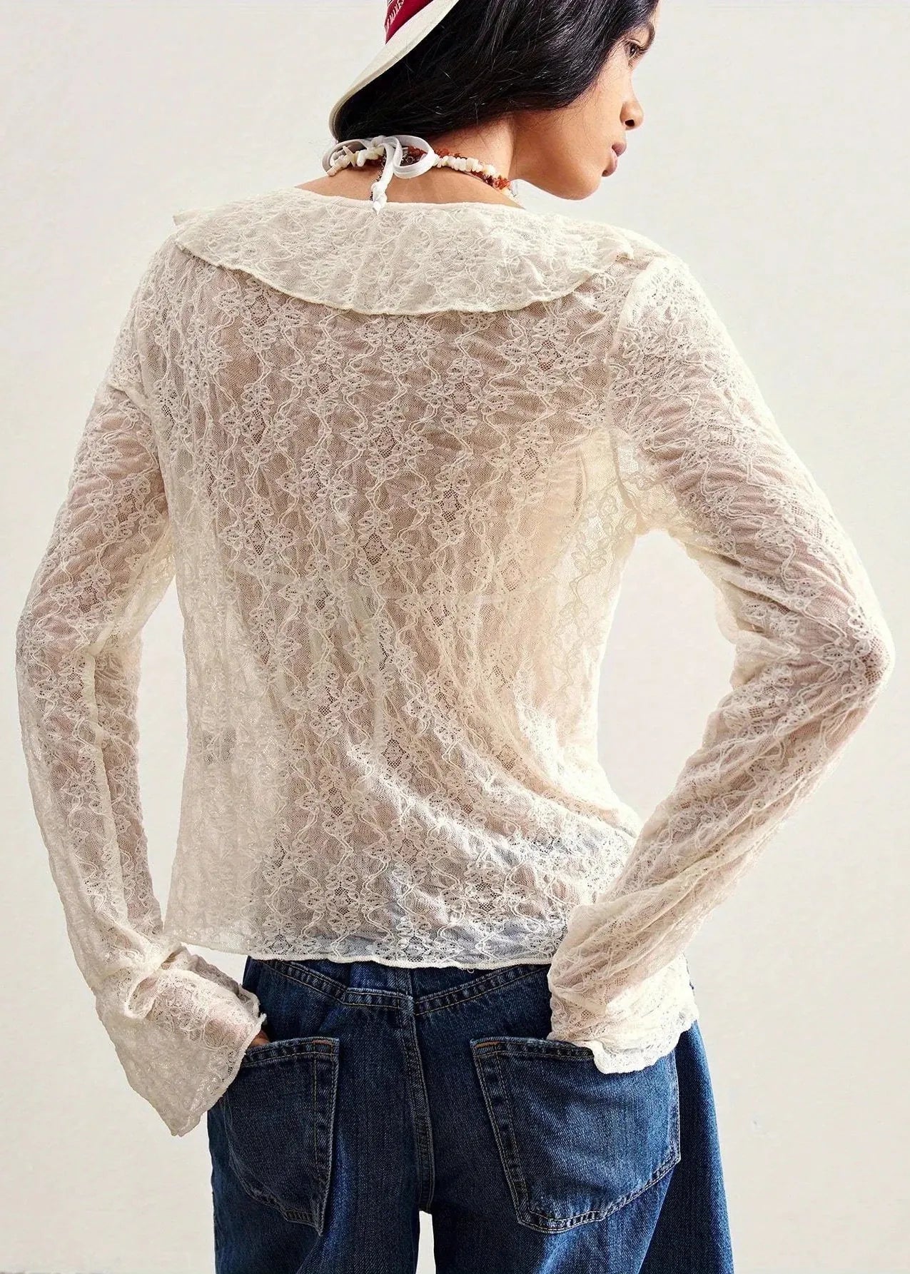 Person wearing a sheer lace top and jeans against a plain background