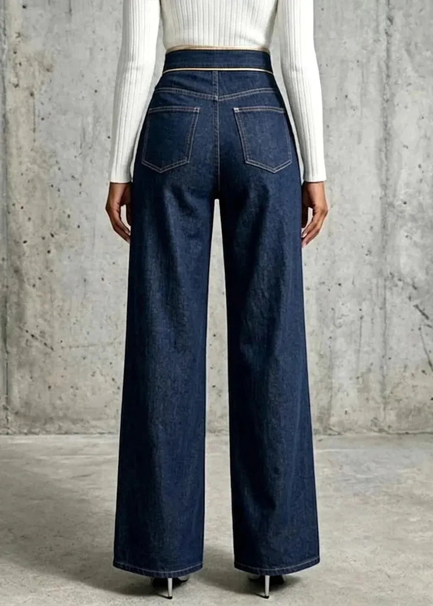 A model shown from the back wearing dark blue wide-leg denim jeans and a white ribbed long-sleeve top, standing against a textured concrete wall.