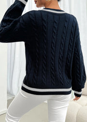 Person wearing a navy blue cable knit sweater with white trim in a minimal indoor setting.