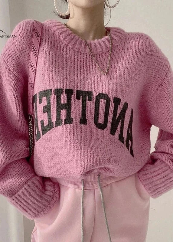 Person wearing a pink sweater with text and matching pants against a neutral background