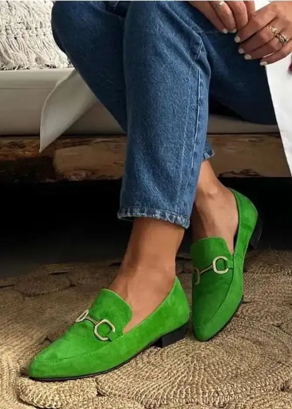 Green loafers worn with blue jeans on a textured rug.