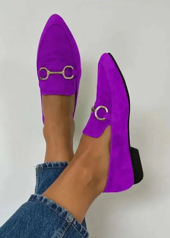Purple loafers with gold buckles worn by a person on a white background