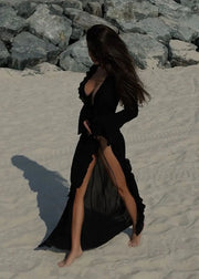 Person wearing a black dress with a high slit on a sandy beach.