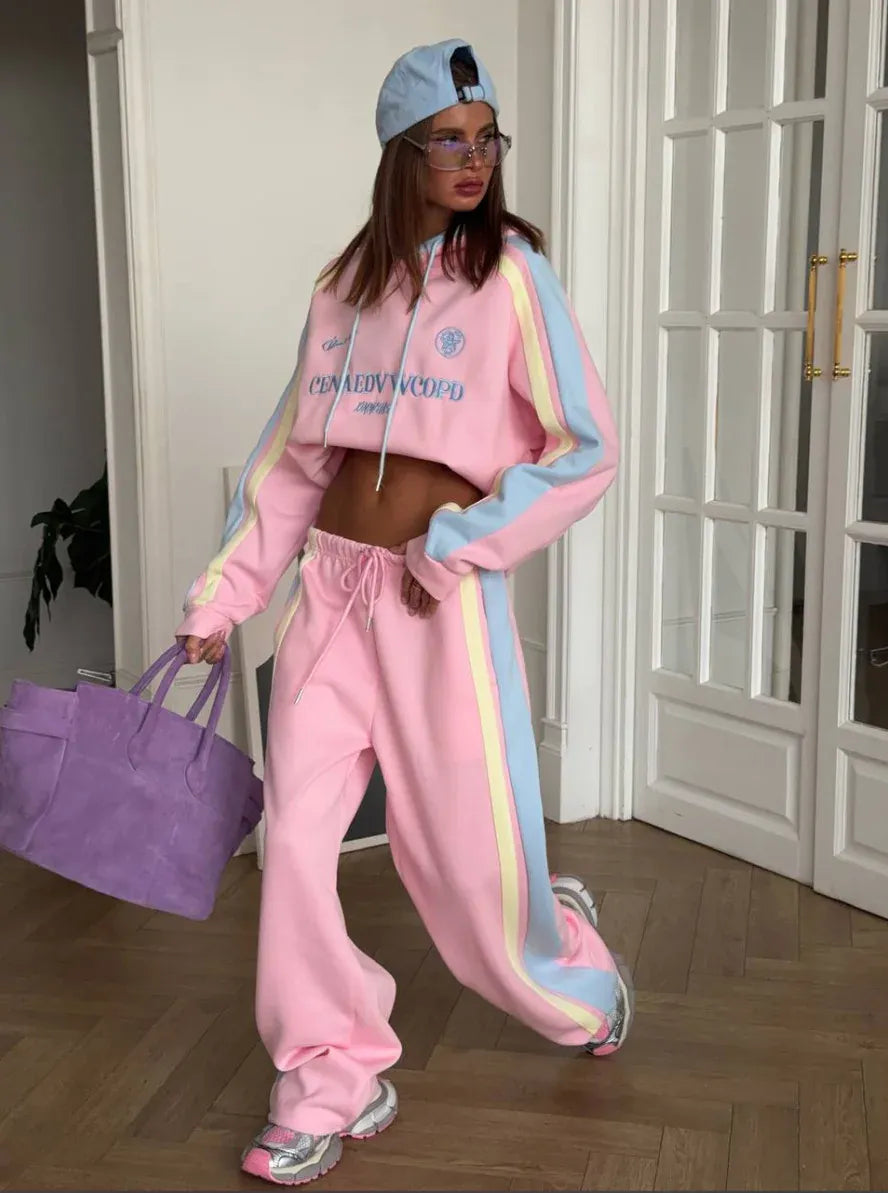 Person wearing a pink tracksuit with colorful stripes, holding a purple bag indoors.