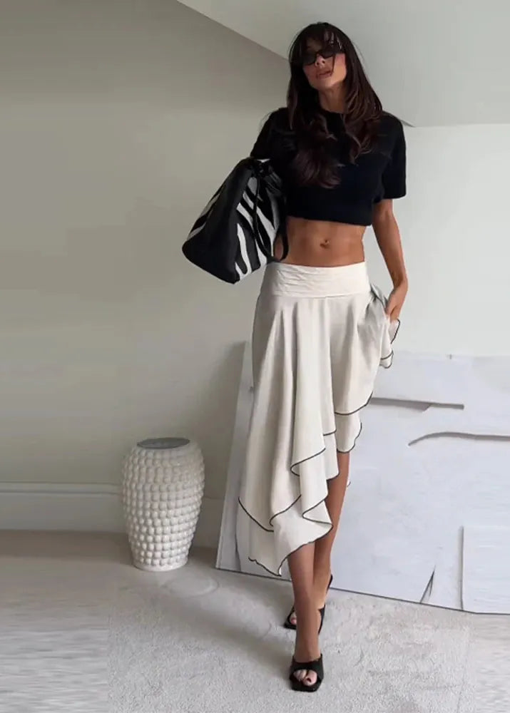 Woman wearing a black top and white skirt in a minimal indoor setting.