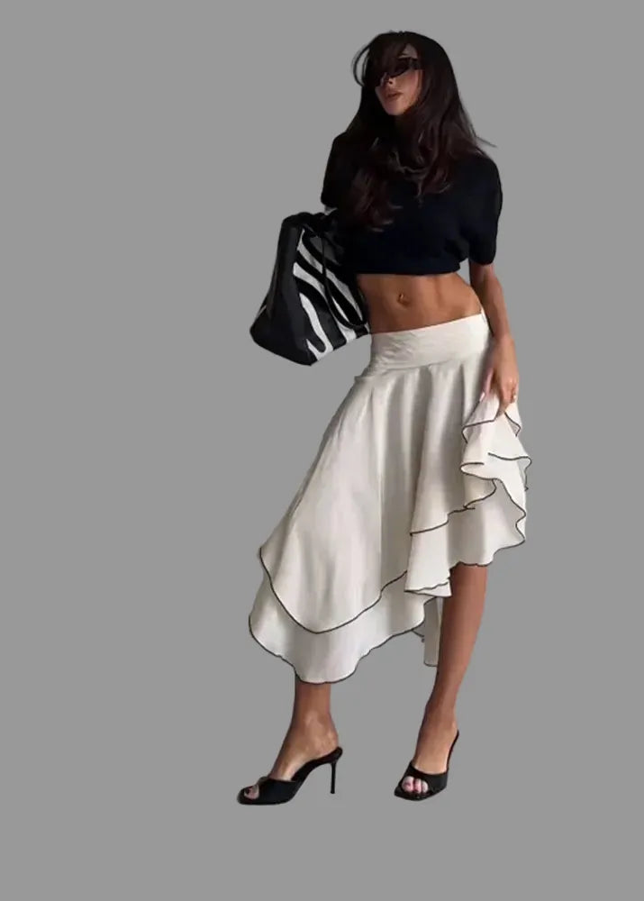 Woman in black crop top and white ruffled skirt standing in a minimalistic room.