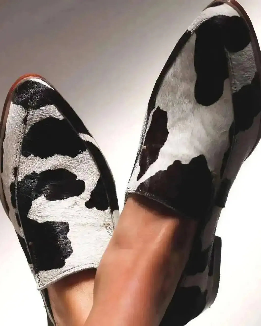 Black and white cow print shoes on a neutral background