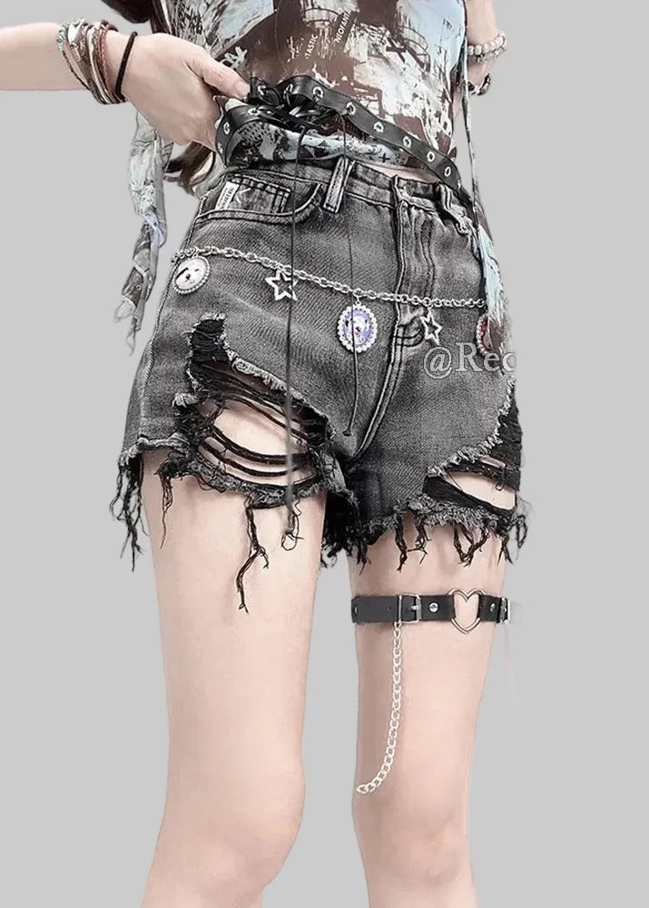 Person wearing ripped denim shorts with decorative chains and embellishments on a plain background