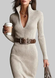Woman wearing a beige ribbed dress with a brown belt, holding a coffee cup against a gray background.
