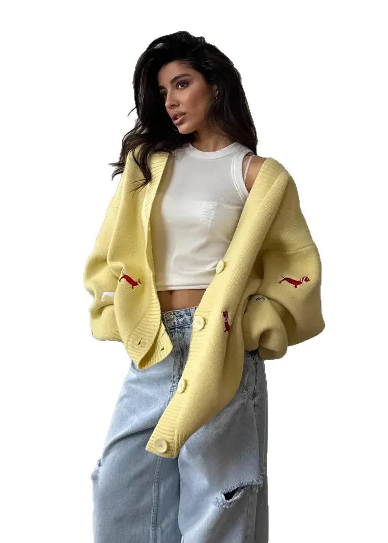 A woman modeling a pale yellow knit cardigan with small red embroidered details, worn open over a white crop top and light blue jeans, against a plain white background.
