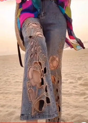 Person wearing jeans with floral embroidery on a beach.