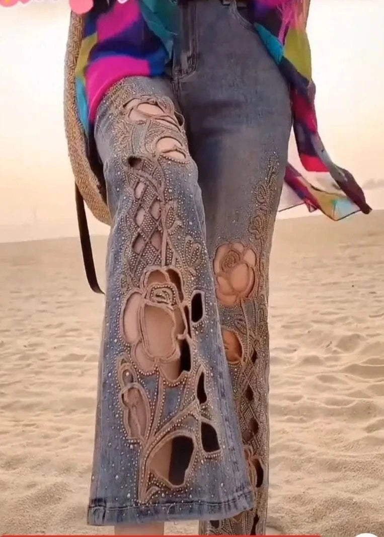 Person wearing jeans with floral embroidery on a beach.