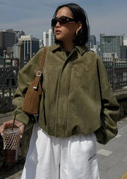 Woman in a green jacket and white pants holding a drink with a cityscape in the background