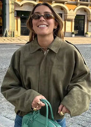 Woman in a green jacket and sunglasses holding a green bag on a street.