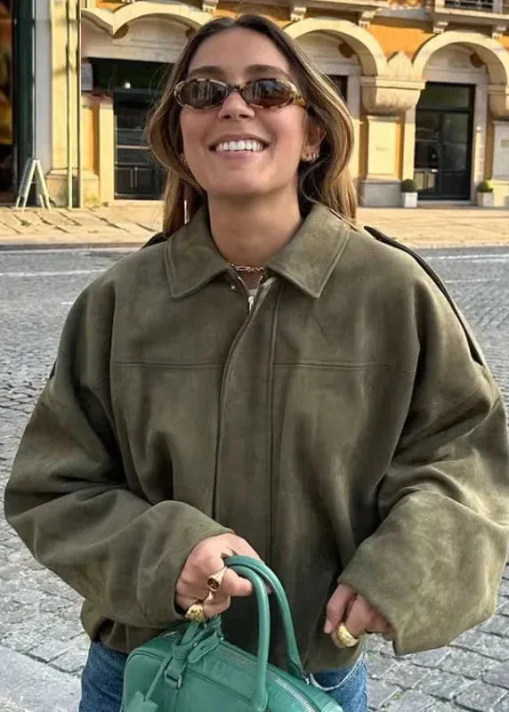 Woman in a green jacket and sunglasses holding a green bag on a street.
