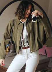 Woman taking a selfie in a green jacket with a camera, sitting on a couch.