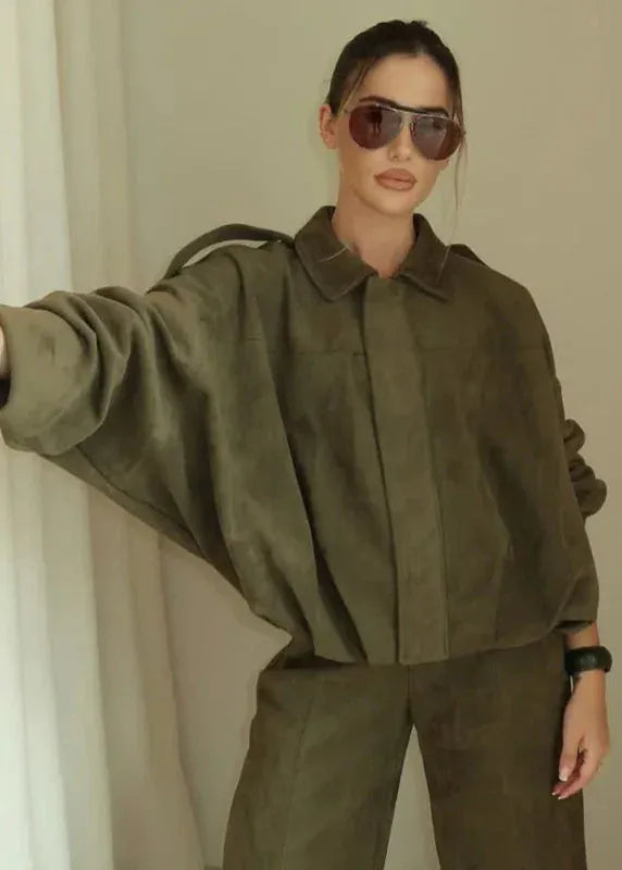 Person wearing an olive green outfit with sunglasses indoors.