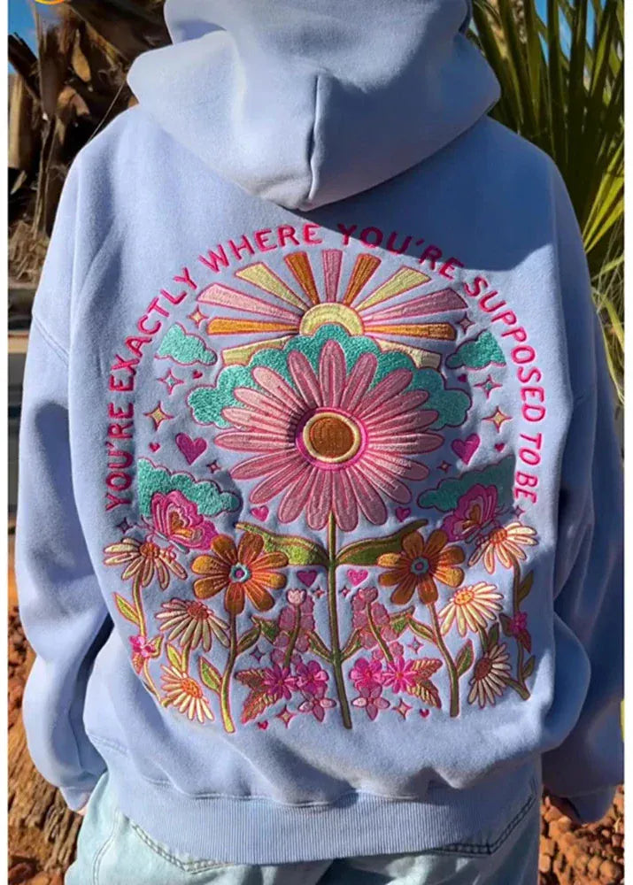 Light blue hoodie with colorful floral design and text on a natural background