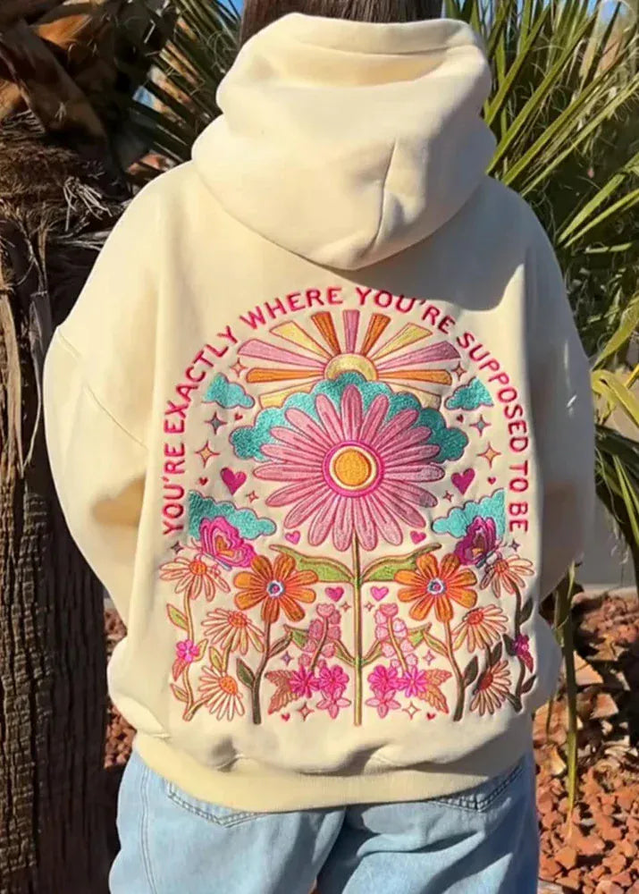 Beige hoodie with colorful floral design and text against a natural background
