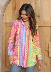 Woman wearing a colorful patterned shirt standing in front of a wooden door.
