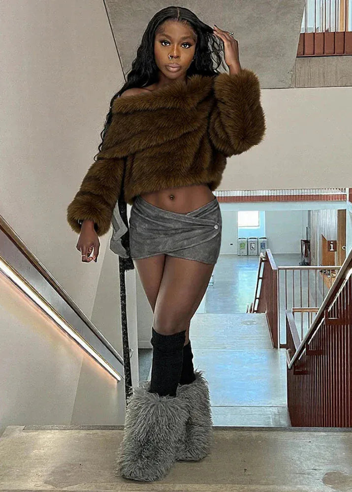 Person wearing a brown fur coat, gray shorts, and gray fuzzy slippers in a modern interior setting.