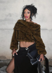 Woman wearing a brown fur coat and black skirt against a textured wall.