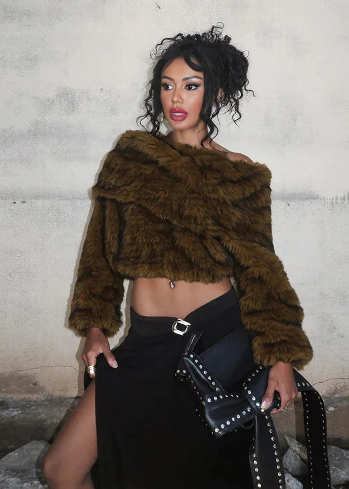 Woman wearing a brown fur coat and black skirt against a textured wall.