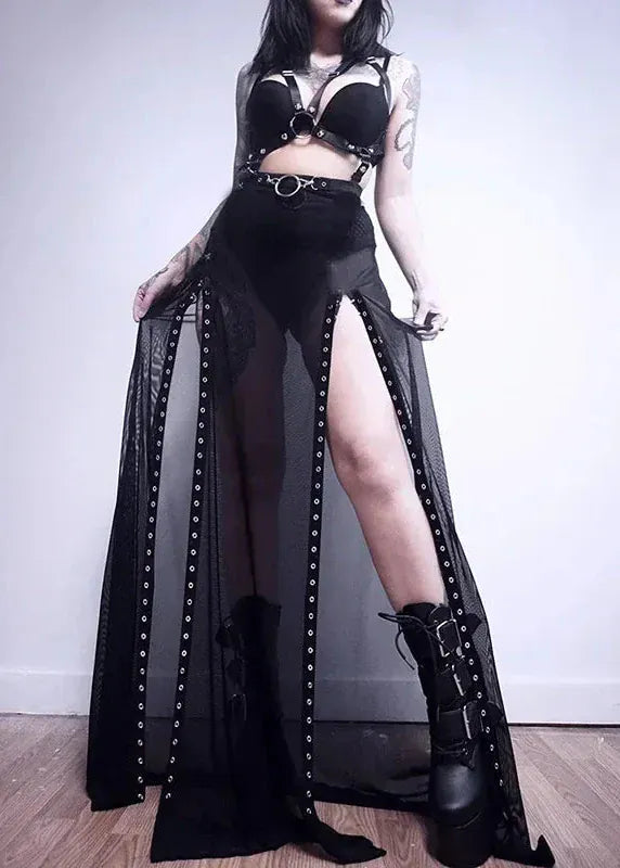 Person wearing a black outfit with high slit skirt and boots against a plain background