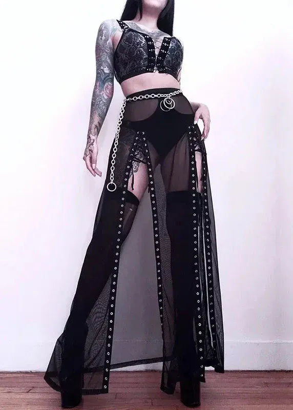 Person wearing a black outfit with sheer panels and high-heeled boots on a plain background