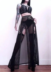 Person wearing a black outfit with sheer panels and high-heeled boots on a plain background