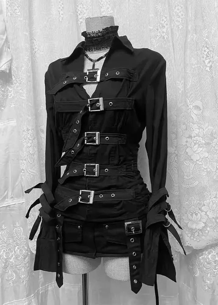 Black gothic-style long-sleeve top and matching shorts set displayed on a mannequin torso, featuring multiple horizontal straps, silver-tone buckles, eyelets, and lace-up details, photographed against a white lace curtain backdrop.