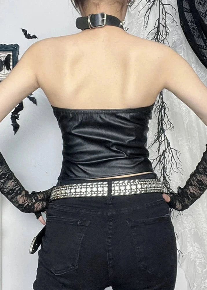 Person wearing a black strapless top and black pants with lace gloves, standing against a decorative background.