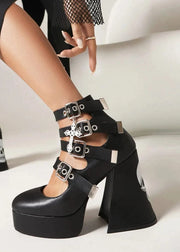 Black platform heels with buckles worn by a person on a neutral background